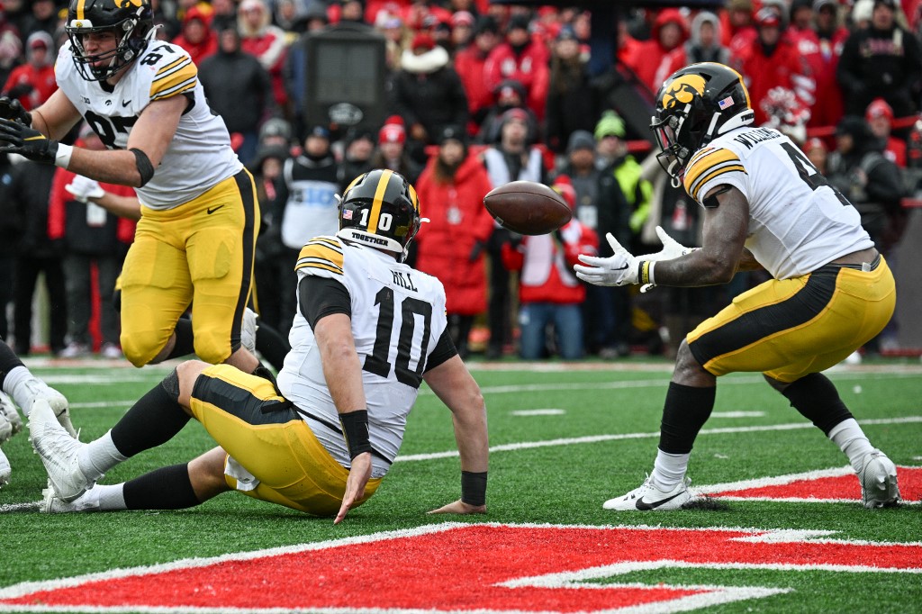 Quarterback Deacon Hill of the Iowa Hawkeyes trips handing off the ball as we share our best Michigan vs. Iowa prediction.