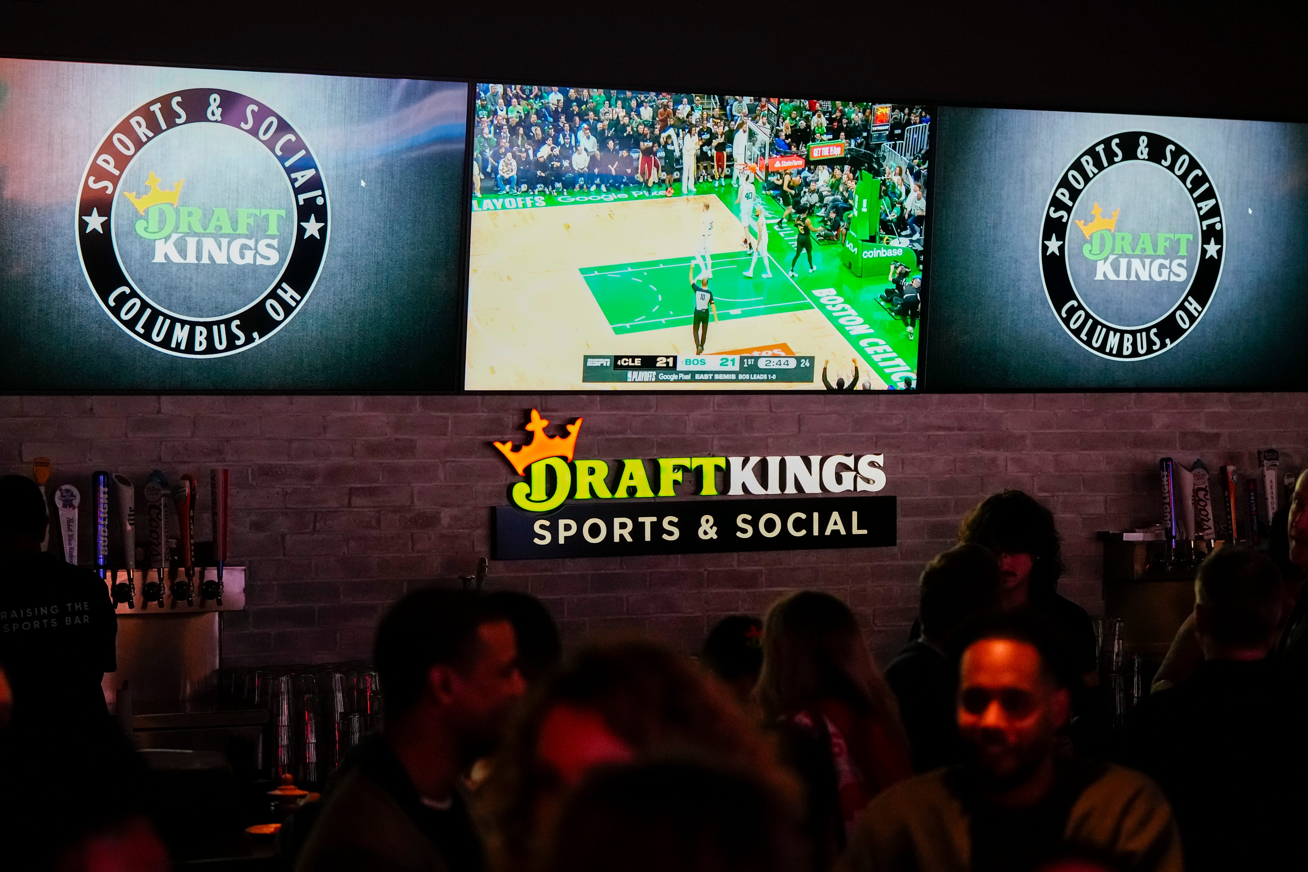 Sports are shown on TVs behind the bar as guests enjoy the grand opening of DraftKings Sports & Social as we look at the fines levied against the sportsbook in New Jersey.