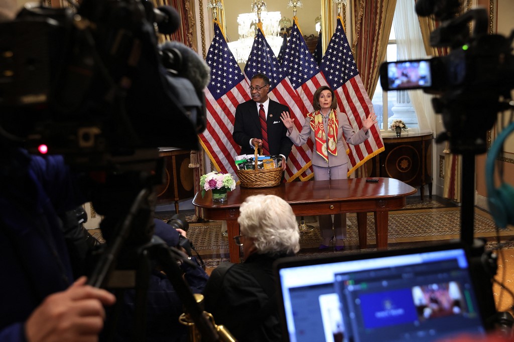 Journalists look on as Speaker of the House Nancy Pelosi (D-CA) presents Rep. Emanuel Cleaver (D-MO) with a basket with items from the San Francisco area, including Ghirardelli chocolate, to settle their friendly wager on the Super Bowl.